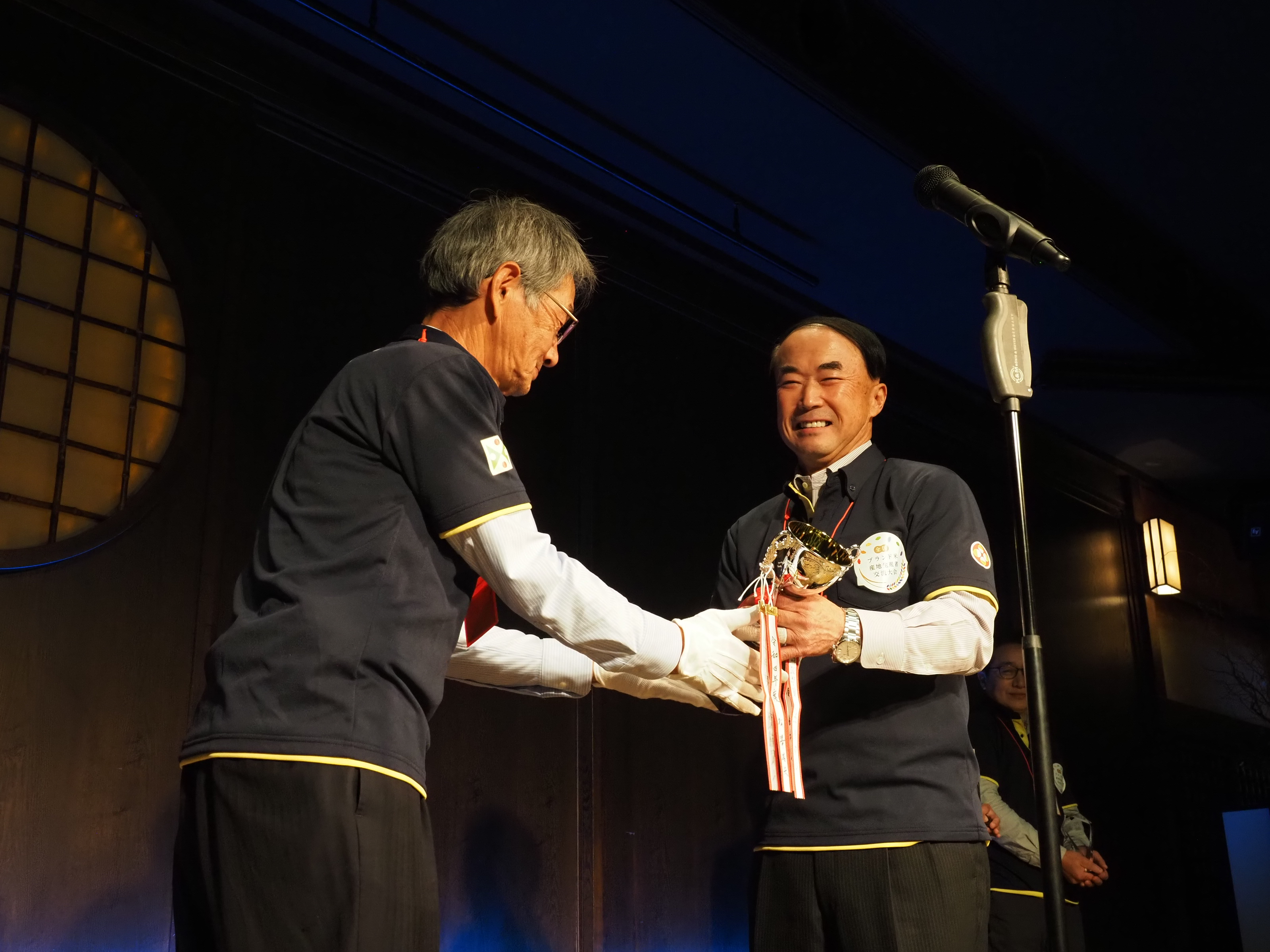 江口会長からトロフィーを受け取る笑顔の遠藤五一マイスター